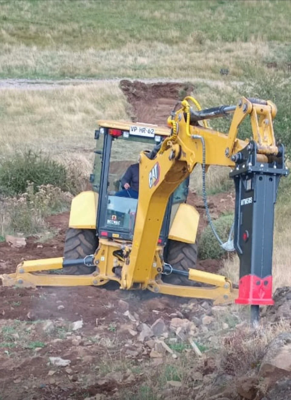 Retroexcavadora CAT 416 con martillo hidráulico perforando roca en Aysén